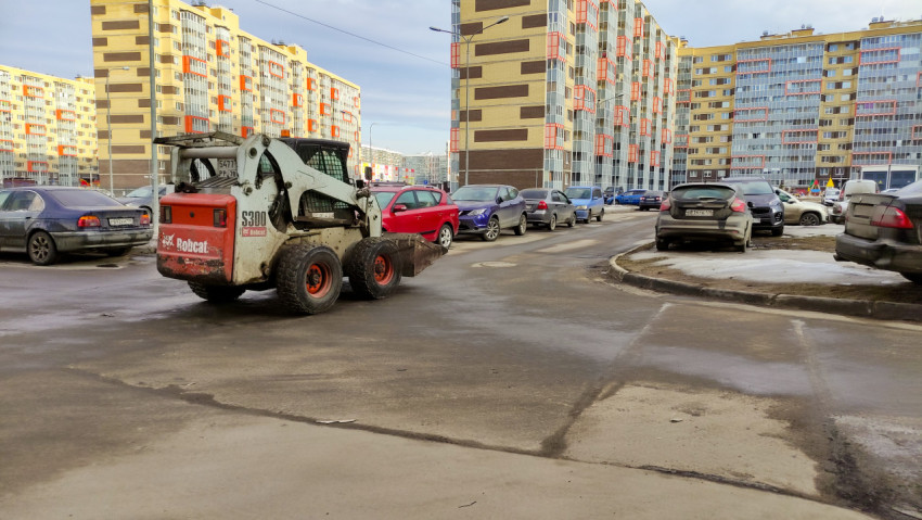 Мини-погрузчик очищает снег во дворе многоквартирного дома