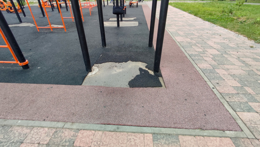 Поврежденные участки резинового покрытия под уличными тренажерами