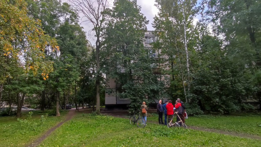 Группа людей на зелёной территории с велосипедами возле жилого дома