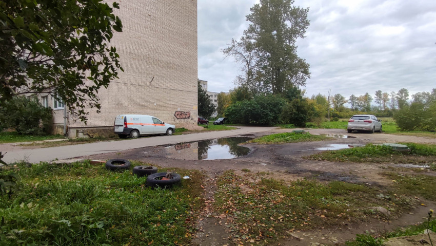 Двор с лужами и припаркованными машинами возле кирпичного дома