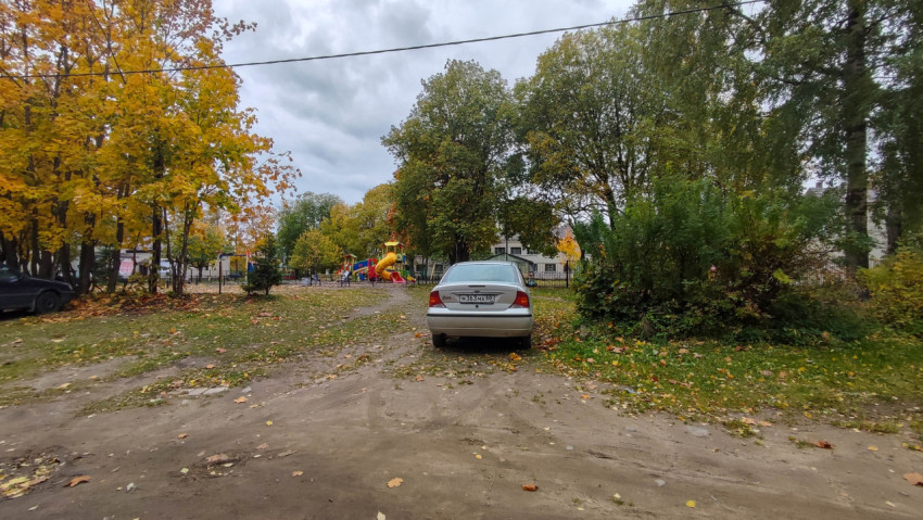 Осенний двор с припаркованной машиной и детской площадкой