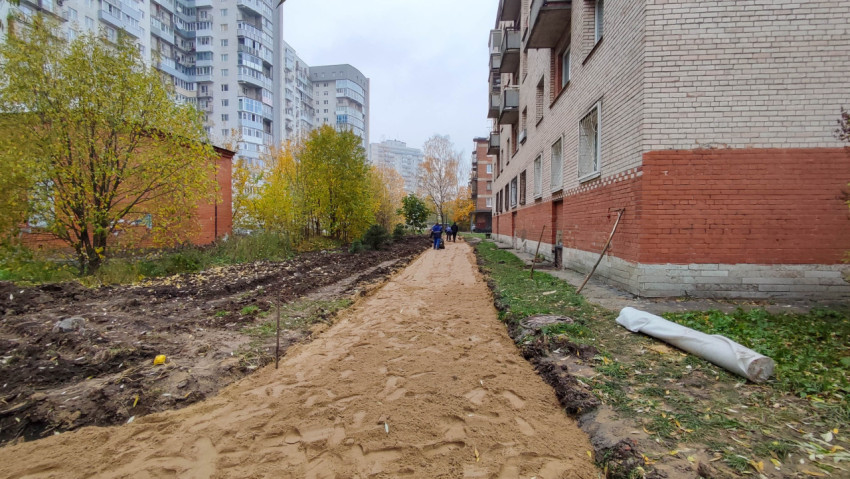Подготовка основания для новой пешеходной дорожки вдоль жилого кирпичного дома