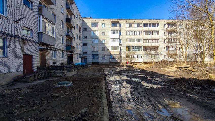 Грязный двор между жилыми домами с лужами и спиленными деревьями