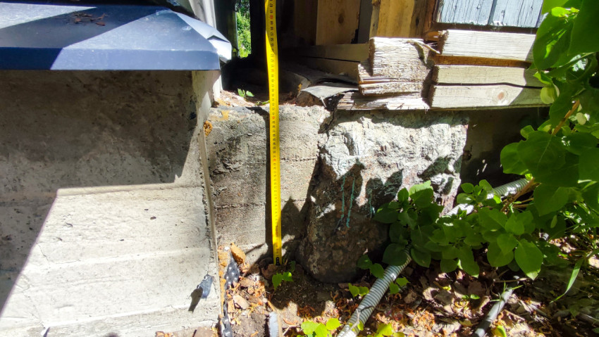 Замер высоты бетонного фундамента рядом с деревянной постройкой