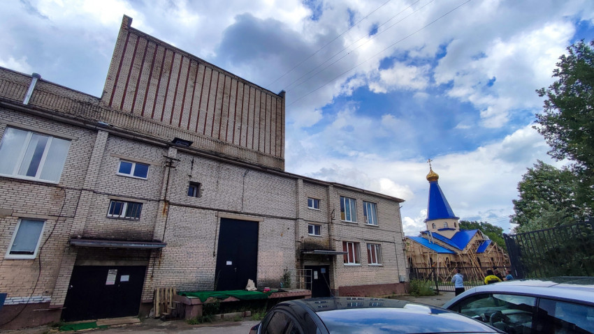 Кирпичное здание с воротами на фоне церкви с голубым куполом