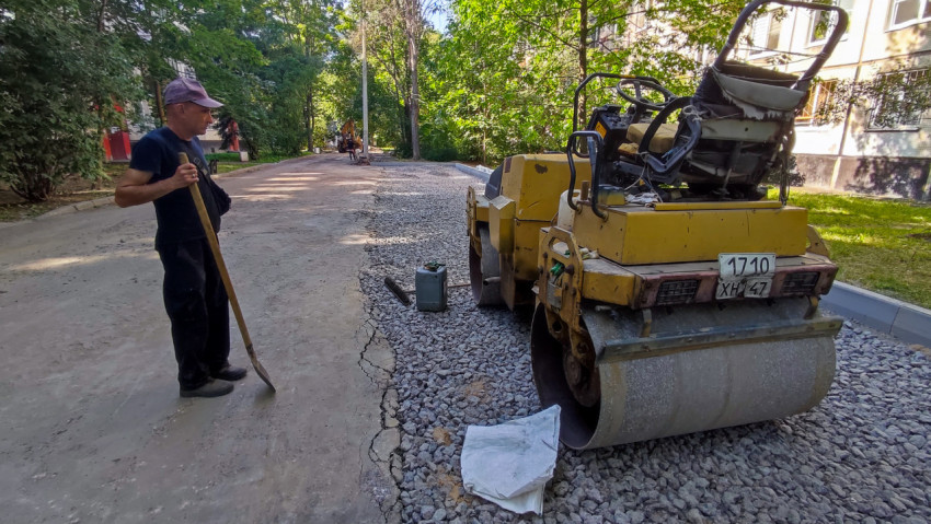 Дорожный каток и рабочие при ремонте дворовой улицы