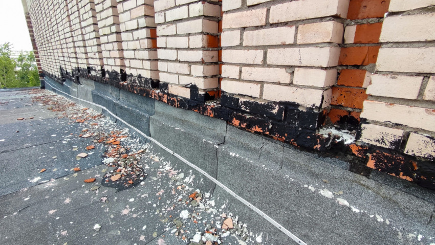 Фасад здания с поврежденной кирпичной кладкой и осыпающимися элементами