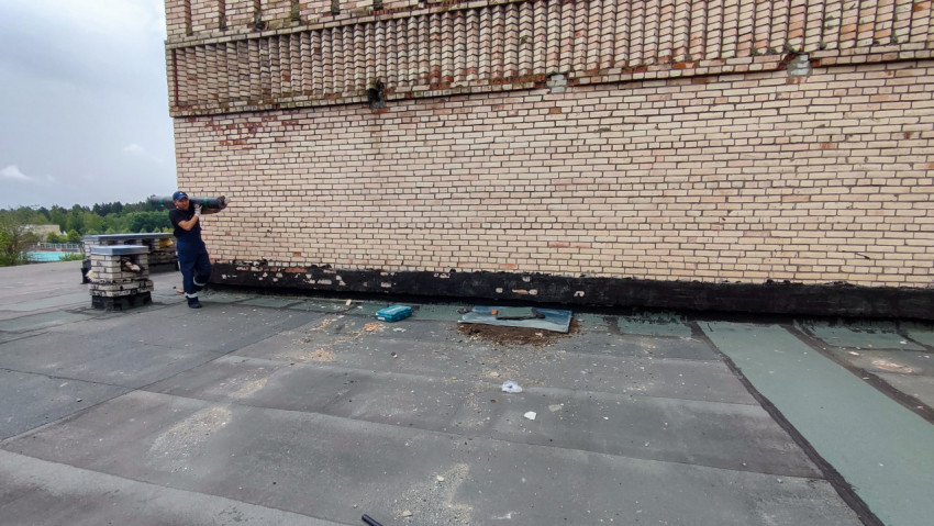 Рабочий несет рулон кровельного покрытия на крыше здания