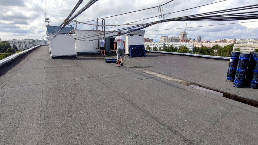 Рабочие и рулоны гидроизоляции на крыше дома