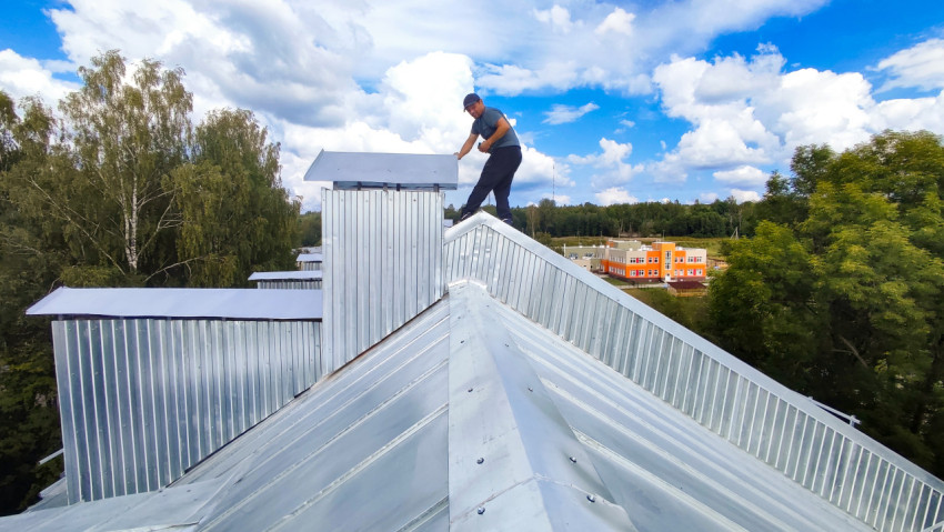 Рабочий на крыше здания с металлической вентиляционной шахтой