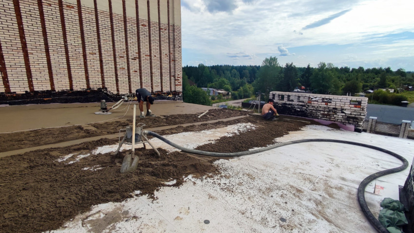 Рабочие выполняют укладку цементной стяжки на крыше