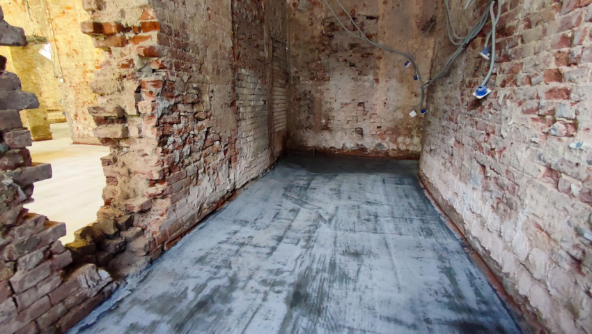 Узкое помещение с повреждённой кирпичной кладкой и новой бетонной стяжкой