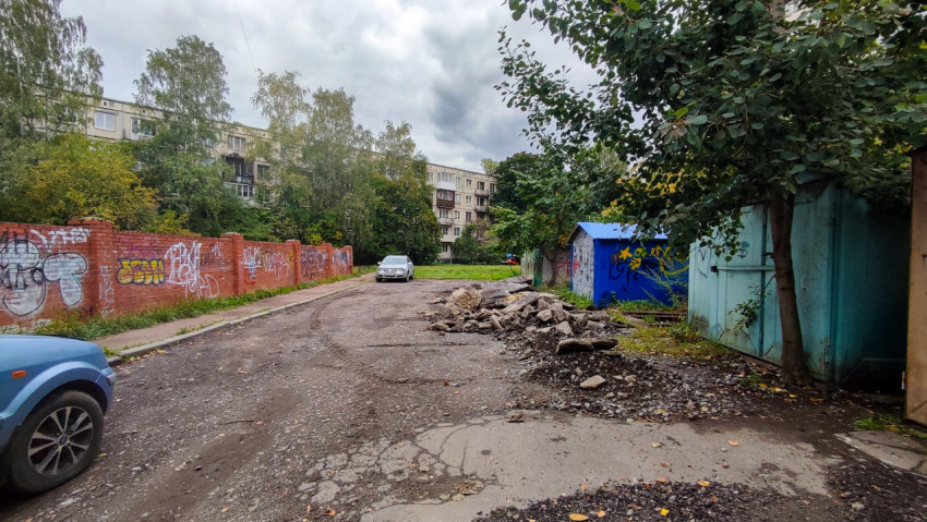 Разбитая асфальтовая площадка у кирпичного забора с граффити