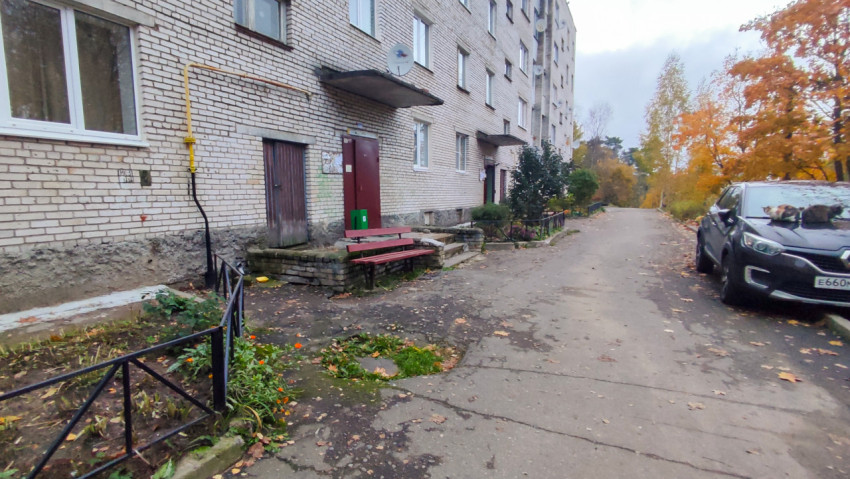 Фасад жилого дома с лавочкой и зелёной урной у подъезда