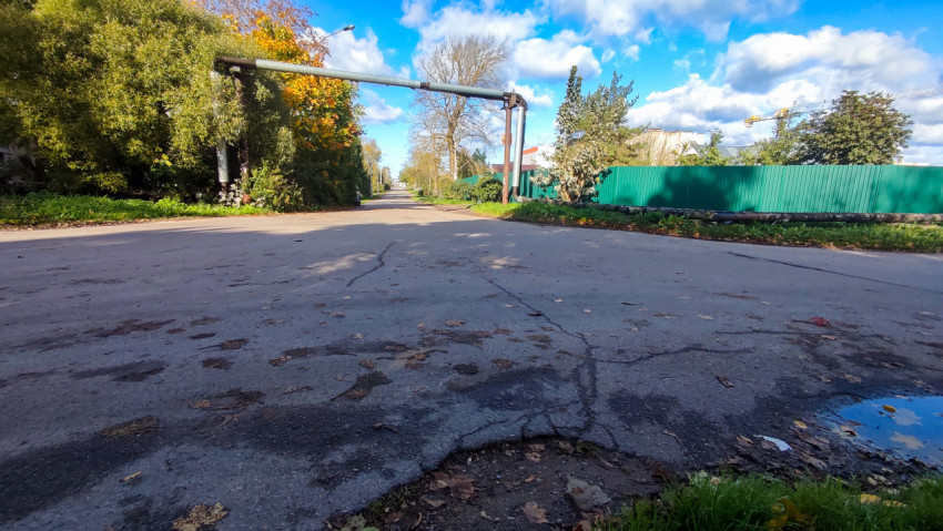 Перекрёсток с трещинами на асфальтовом покрытии и воздушным трубопроводом