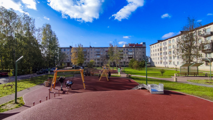 Детская площадка с качелями и горкой на фоне жилых домов
