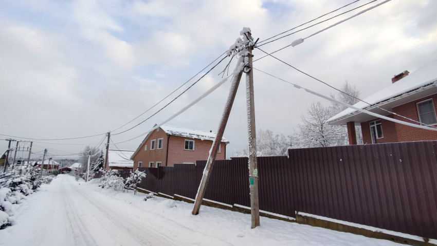 Опора воздушной линии связи с налипшим снегом вдоль загородной улицы