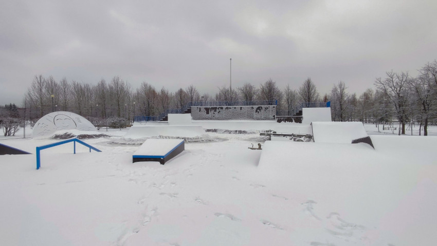 Общий вид скейтпарка зимой с заснеженными фигурами и рампами