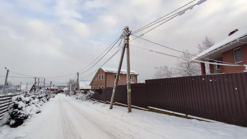 Узкая улица частного сектора с опорами линии электропередачи зимой
