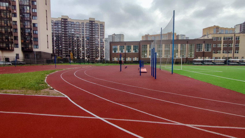 Беговые дорожки и футбольное поле у школьного здания в жилом районе