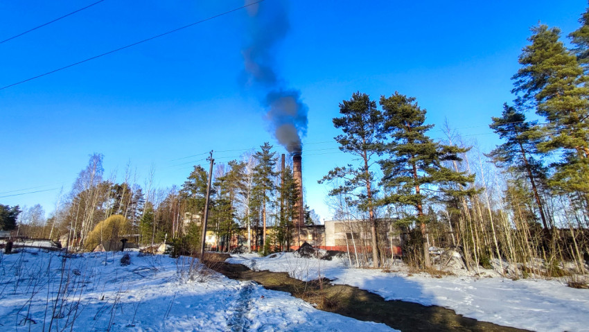 Заводская труба с дымом среди заснеженного леса