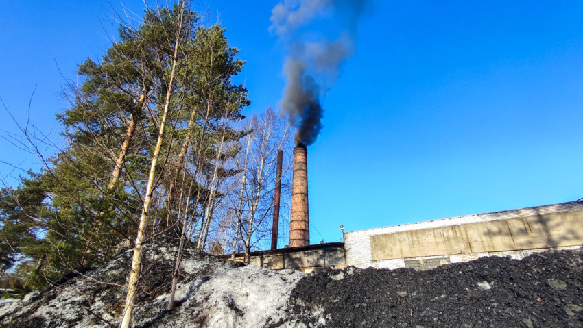 Заводская труба с черным дымом и остатками снега на переднем плане