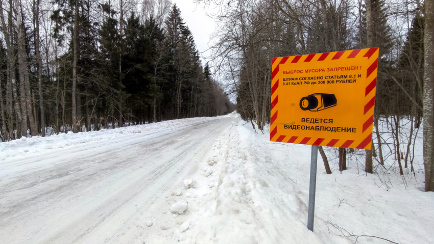 Знак «Выброс мусора запрещен» на заснеженной дороге через лес