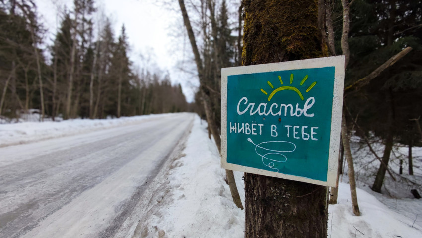Табличка с надписью «Счастье живёт в тебе» на заснеженной лесной дороге