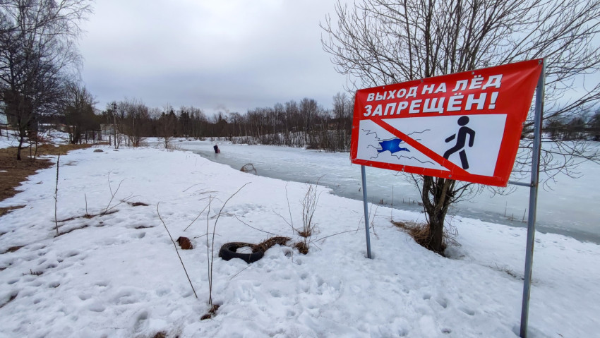 Предупреждающий знак у заснеженного берега пруда зимой