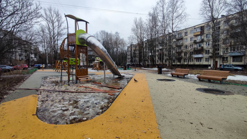 Детская площадка с горкой и лавками во дворе панельных домов