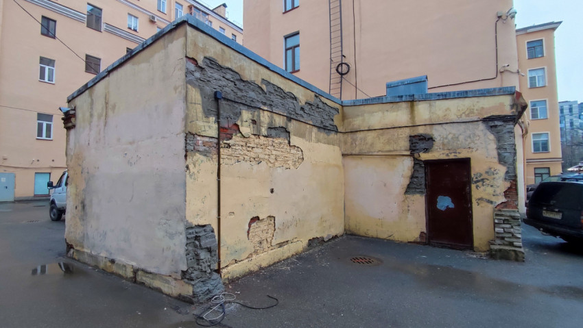 Обветшавшая стена хозяйственного строения с повреждённой штукатуркой