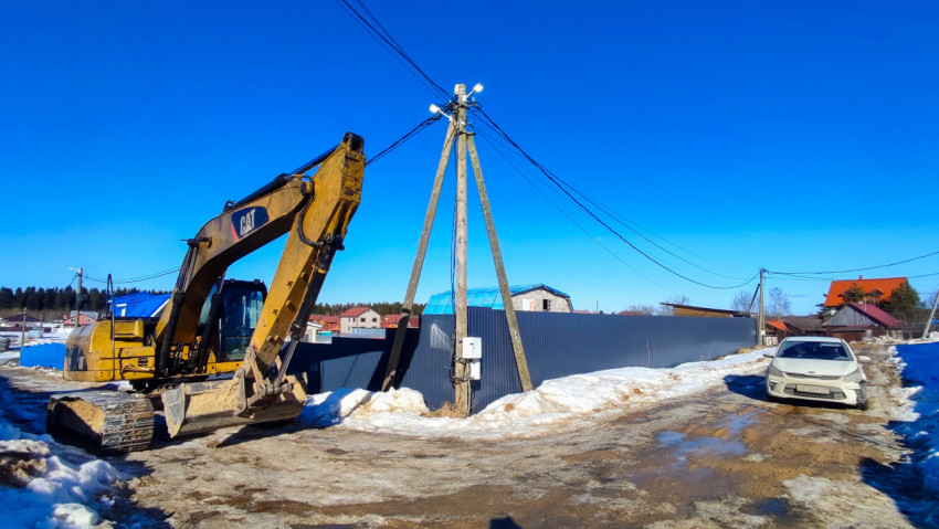Экскаватор возле опоры электросети на загородной улице