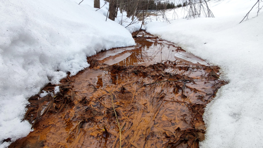Узкий ручей с талой водой среди снежных склонов
