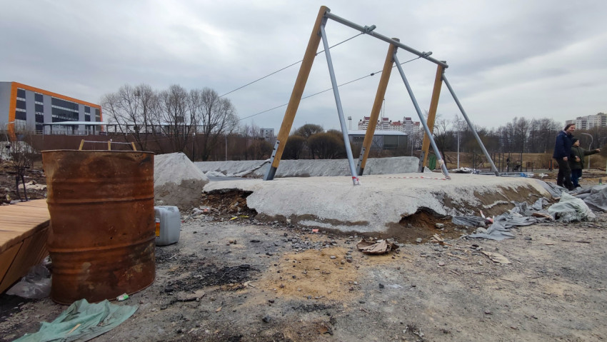 Недостроенная зона отдыха с качелями и ржавой бочкой на фоне современного здания