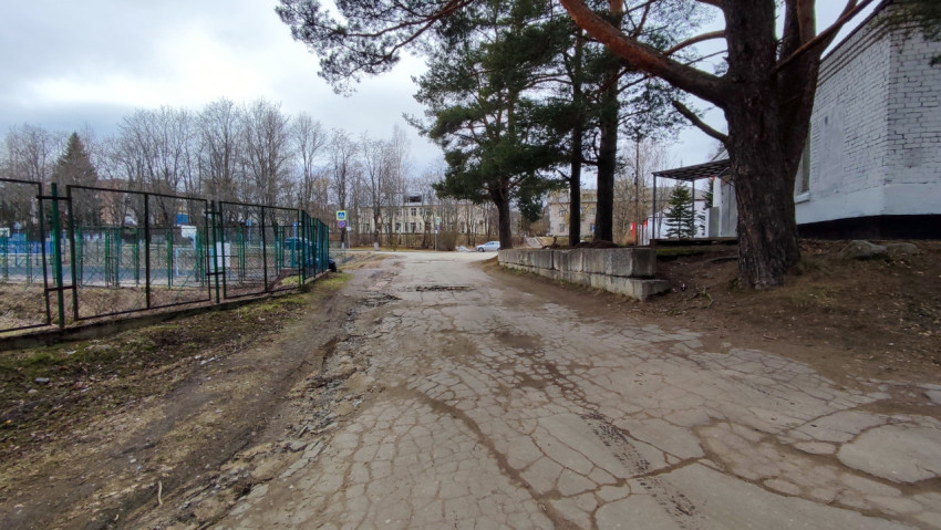 Старая дорога вдоль ограждения спортивной территории в окружении деревьев