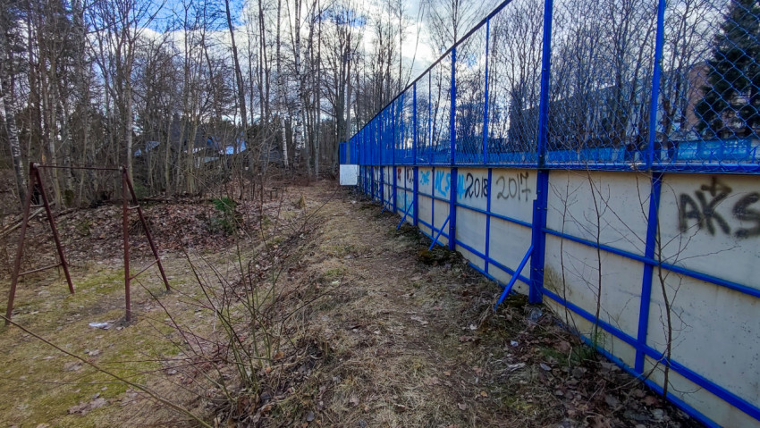 Тропинка вдоль ограждения спортивной площадки у лесного массива