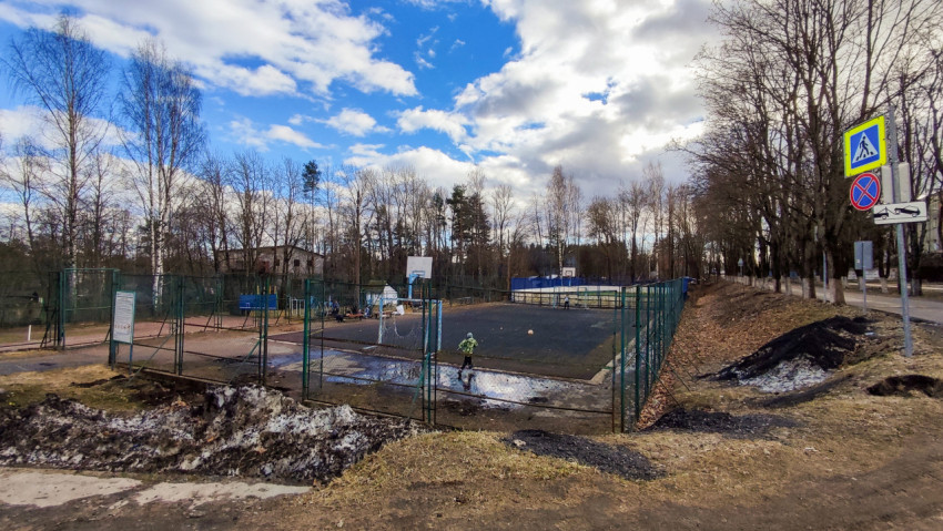Спортивная площадка с ограждением и дорожными знаками на фоне весеннего неба