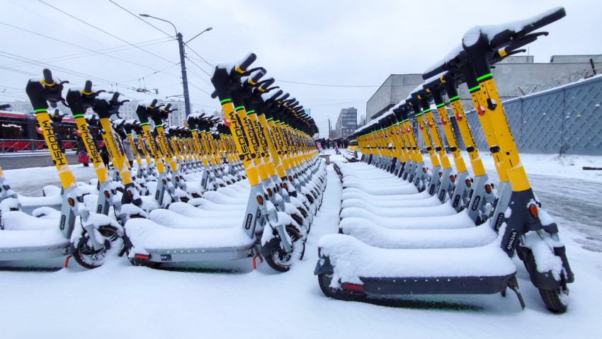 Ряды снежных электросамокатов на фоне городской застройки
