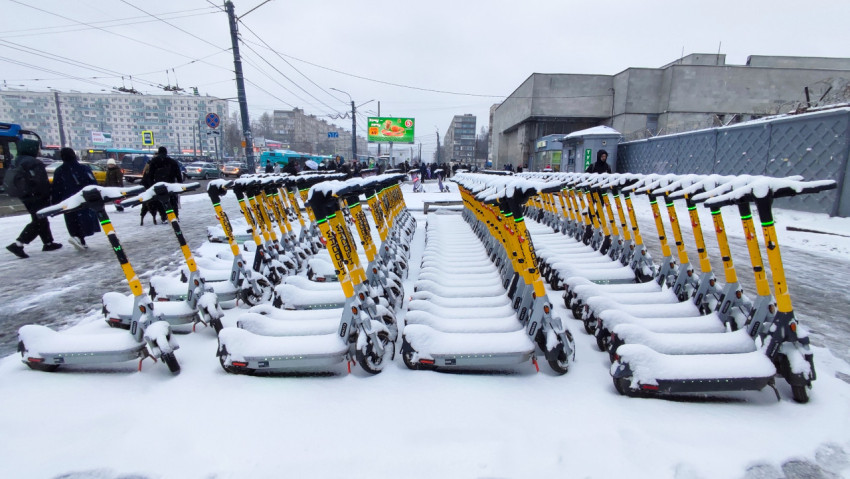 Зимняя парковка электросамокатов на фоне оживлённого перекрёстка