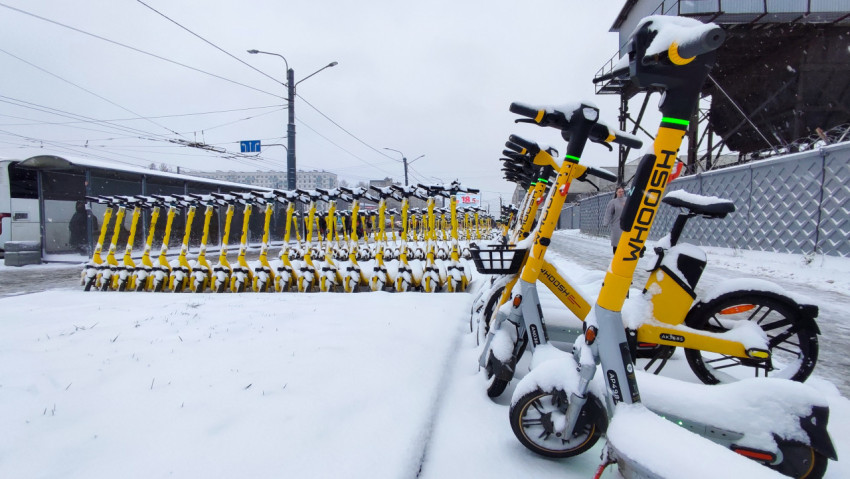 Электросамокаты и велосипеды Whoosh под снегом у городской промышленной стены