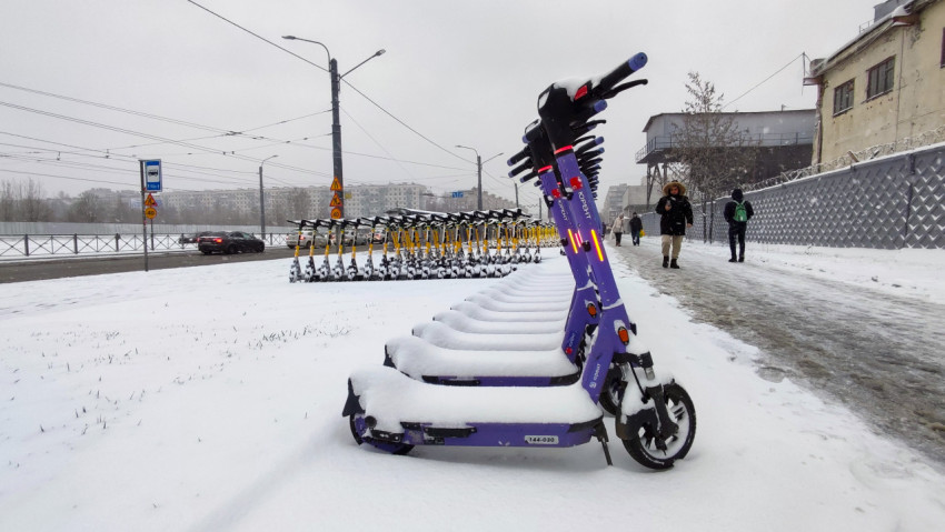 Фиолетовые электросамокаты Юрент под снегом вдоль городского тротуара