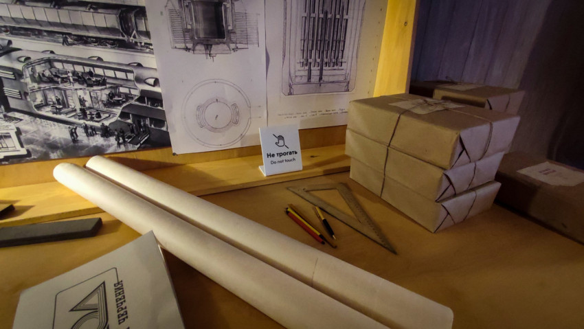 Рулоны бумаги, карандаши и чертёжный угольник у стенда с техническими схемами