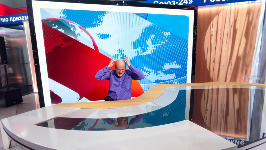 Мужчина у демонстрационного новостного стола на фоне крупной медиа-графики