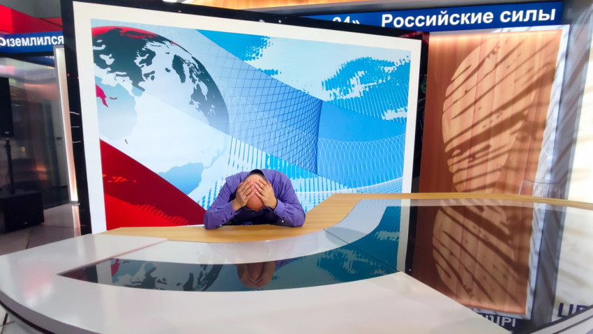 Мужчина за новостным столом демонстрационной студии на фоне глобальной графики