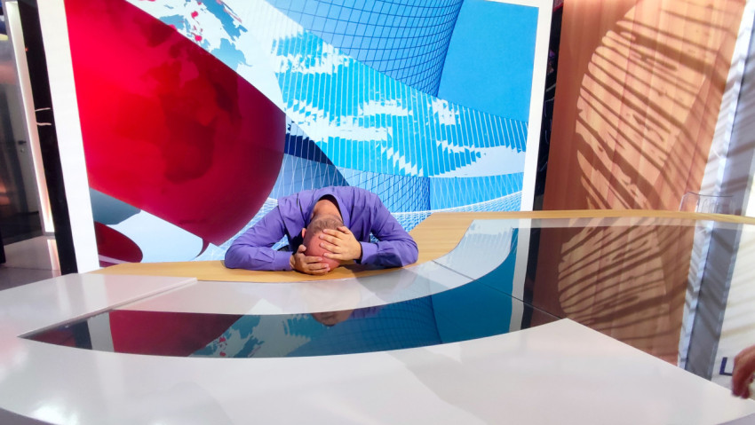 Посетитель демонстрационной телестудии за новостным столом с проекционной графикой