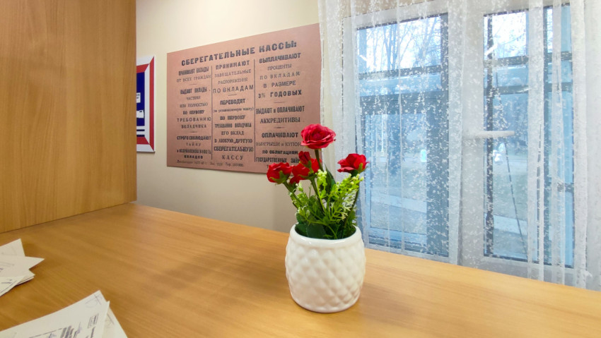 Стена с информационным плакатом сберегательных касс и ваза с цветами