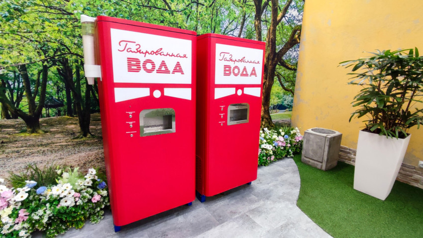 Автоматы газированной воды в декоративной зоне с растениями и жёлтой стеной