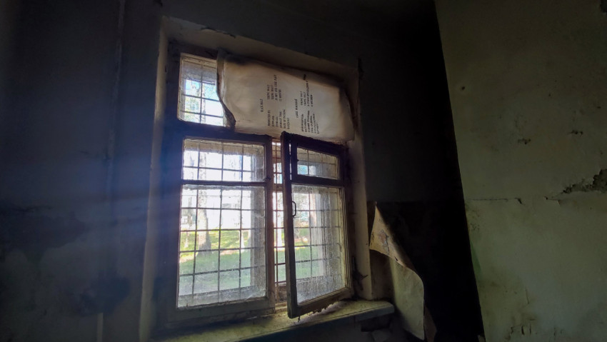 Окно с решеткой и поврежденной отделкой стен в старом помещении