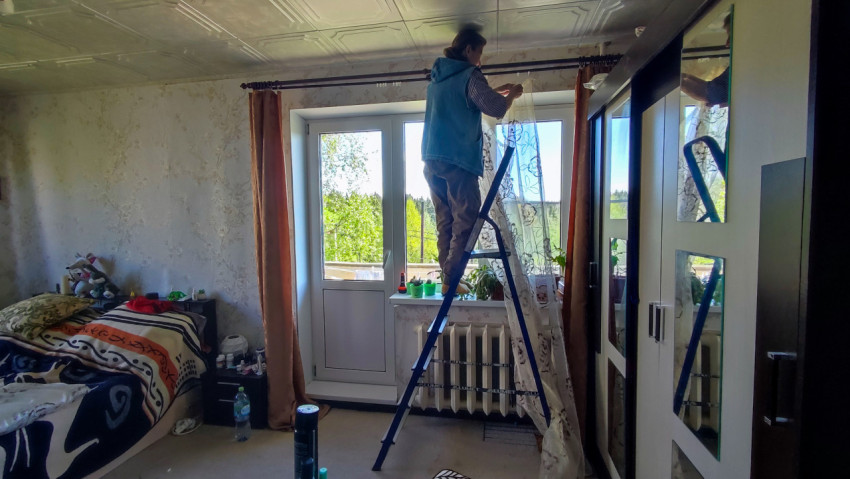 Женщина на стремянке крепит тюль на карниз в спальне