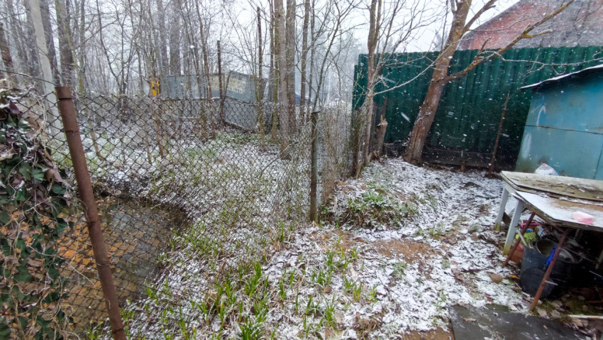 Сетчатый забор и заросшая территория у ручья во время снегопада